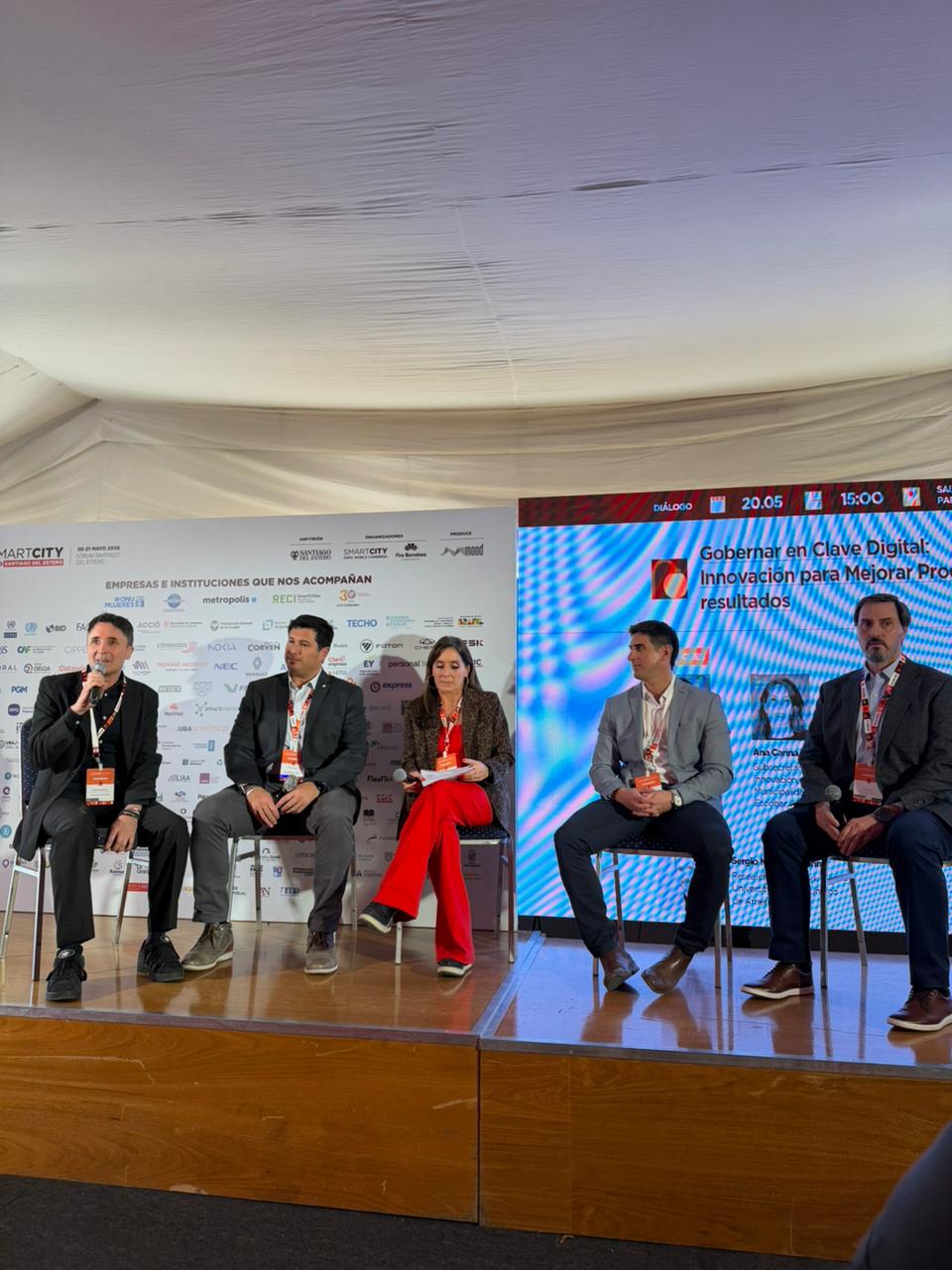 On-stage moderation: Sergio Mastrogiovanni opens the panel 'Gobernar en Clave Digital' with the projected backdrop visible behind, flanked by four panelists.